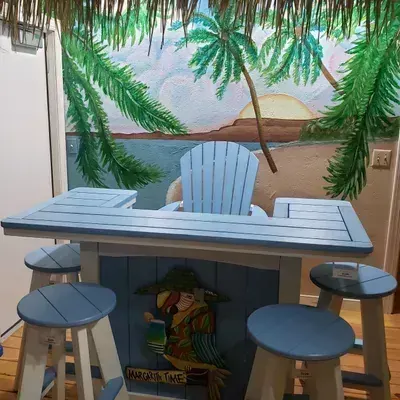 Gray poly outdoor bar and stools in front of a palm-tree mural